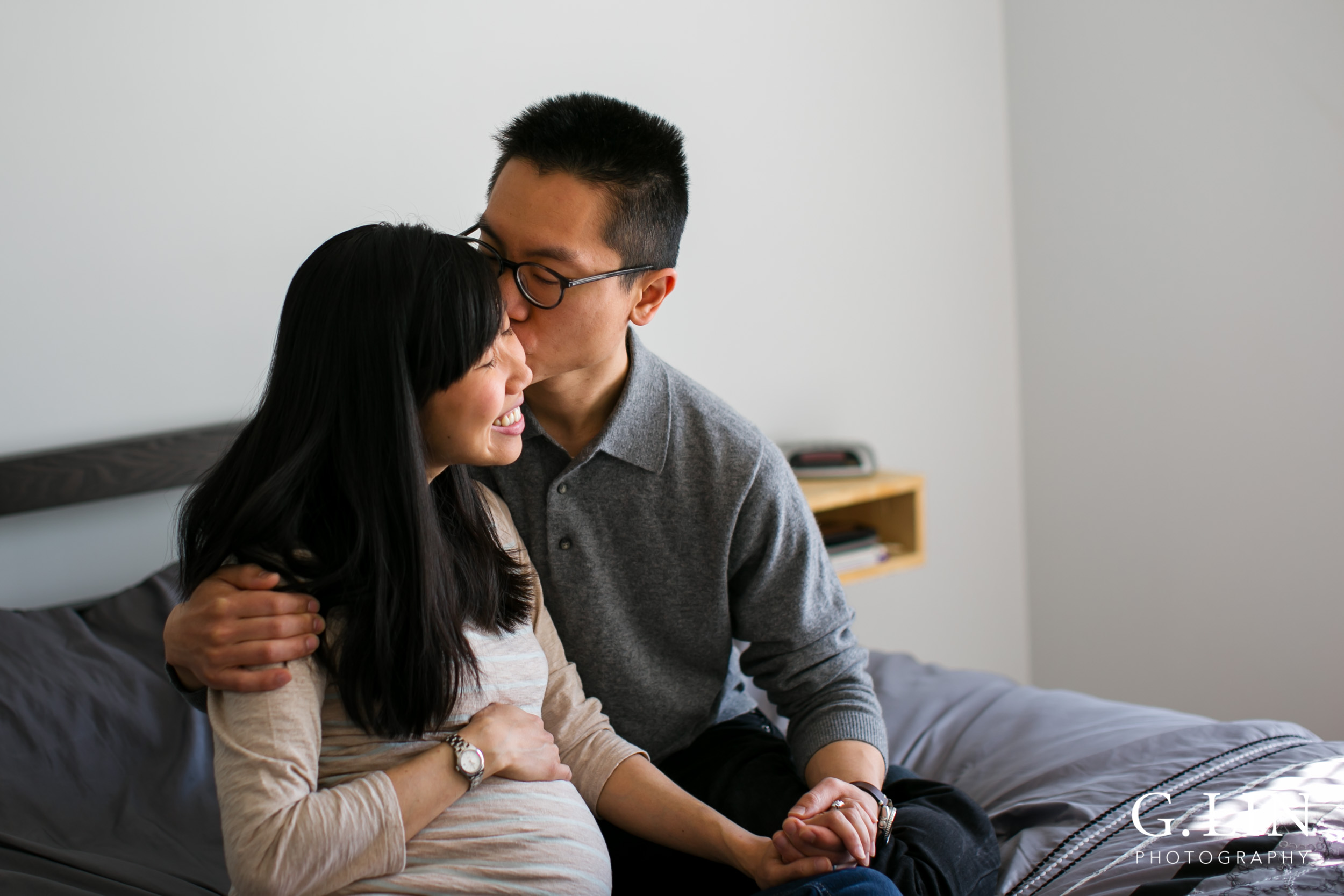 Durham Maternity Photography | G. Lin Photography | Husband kissing wife on cheek sitting on bed