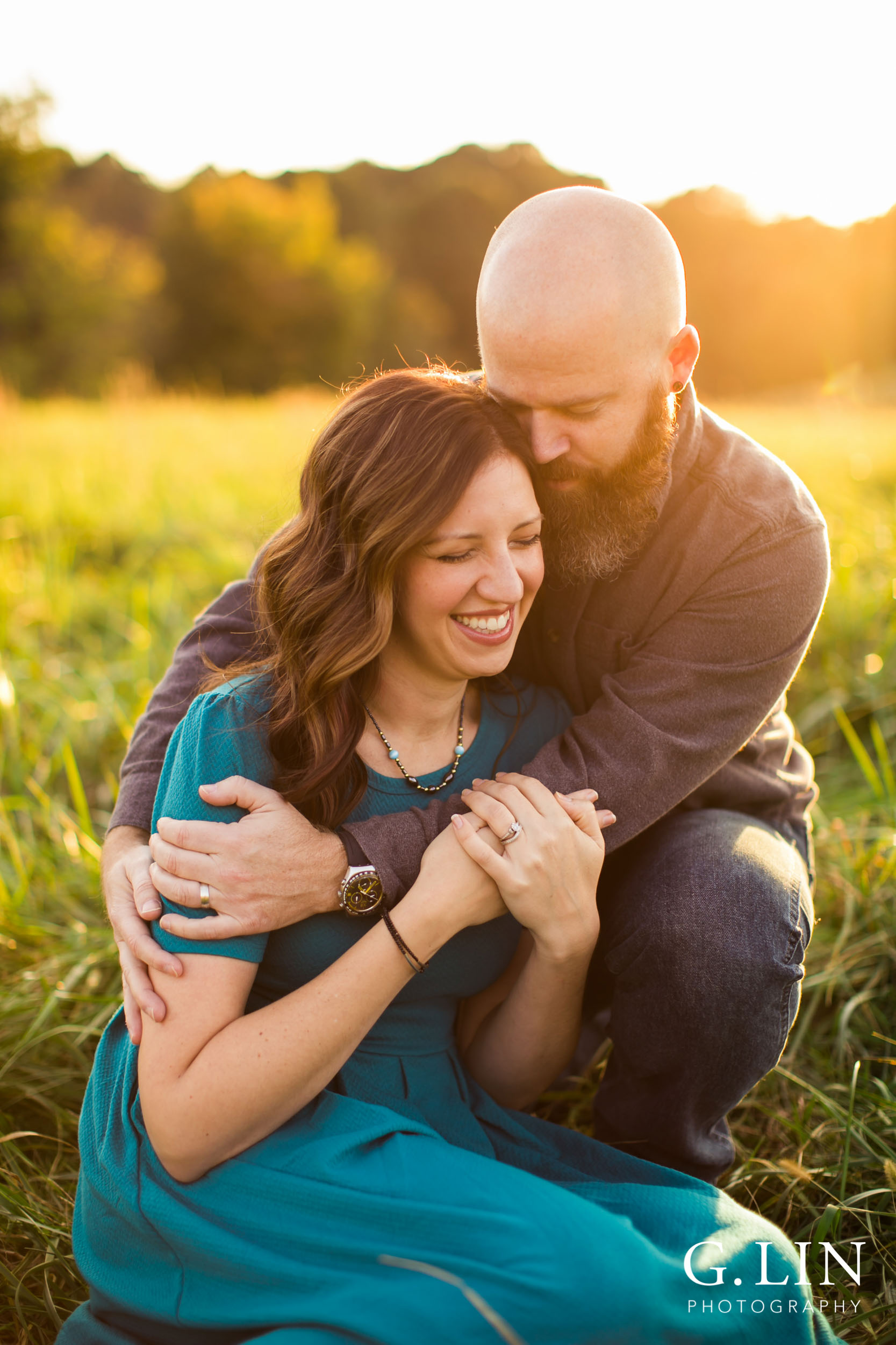 Couple laughing with each other sitting in open field during sunset | Raleigh Family Photographer | G. Lin Photography