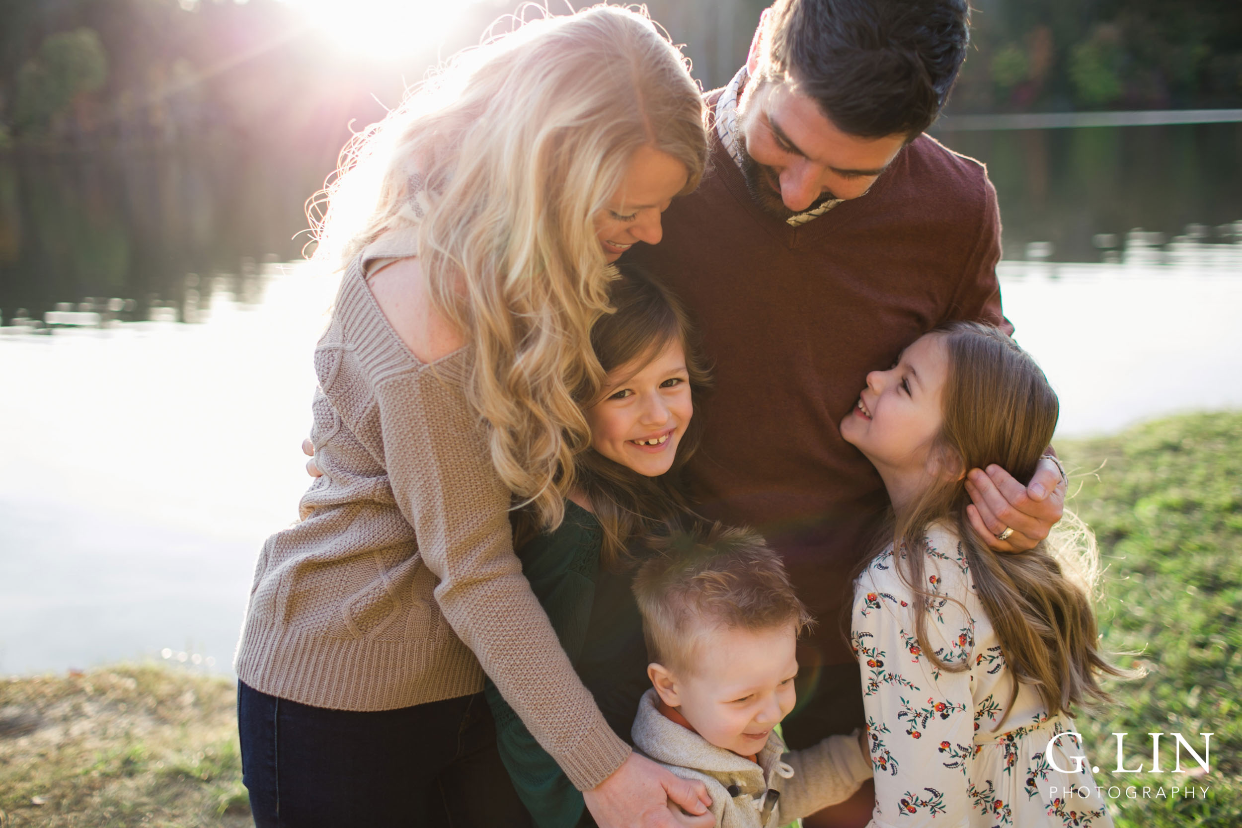 Raleigh Family Photographer | G. Lin Photography | Candid photo of family looking at each other and smiling by the lake during golden hour