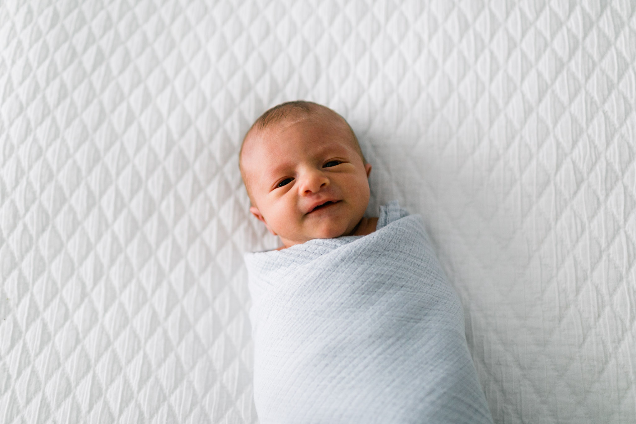 Baby boy on white bed smiling | Durham Newborn Photographer | By G. Lin Photography