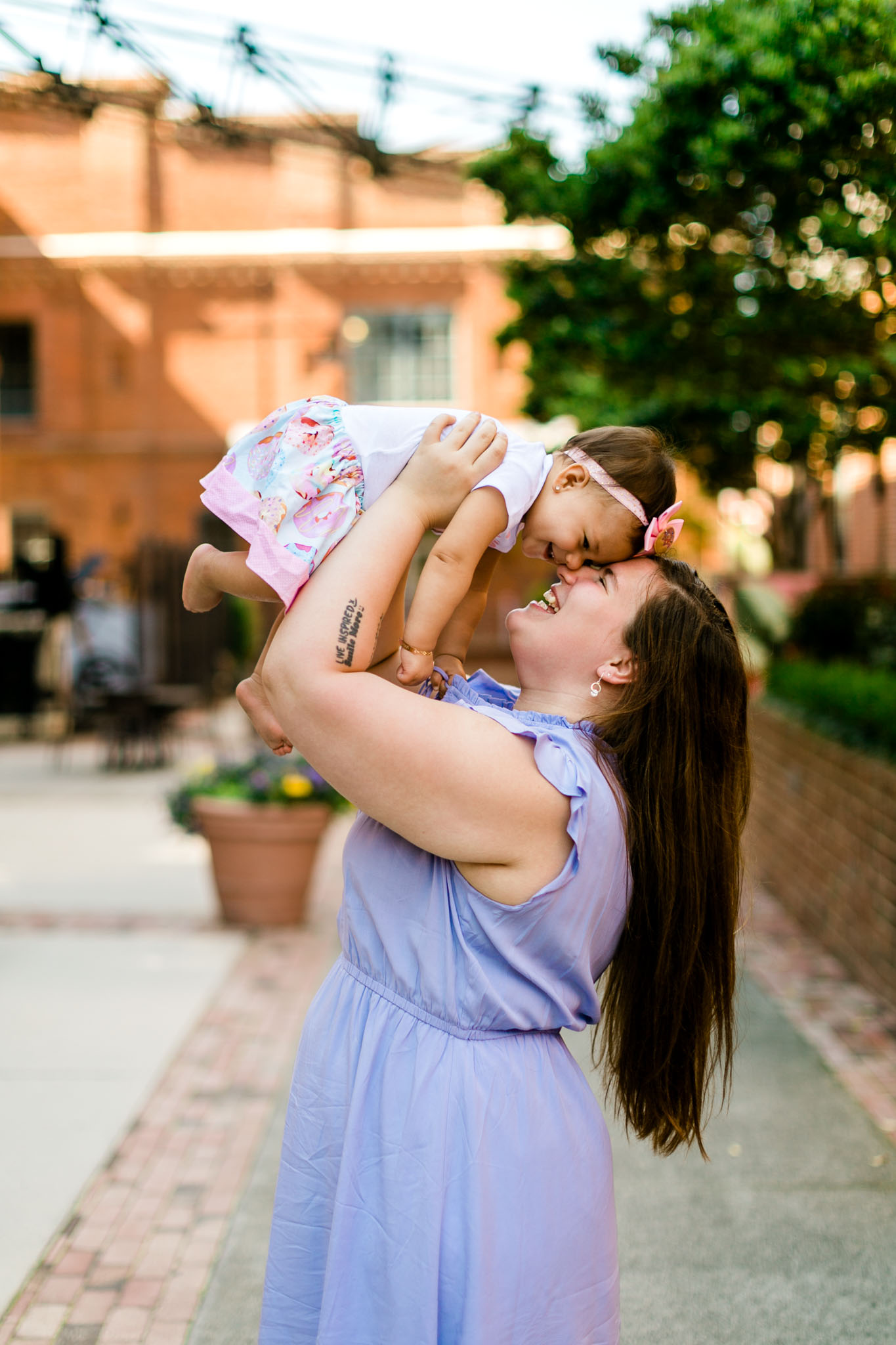 Mother holding baby girl in the air at American Tobacco Campus | Durham Photographer | By G. Lin Photography