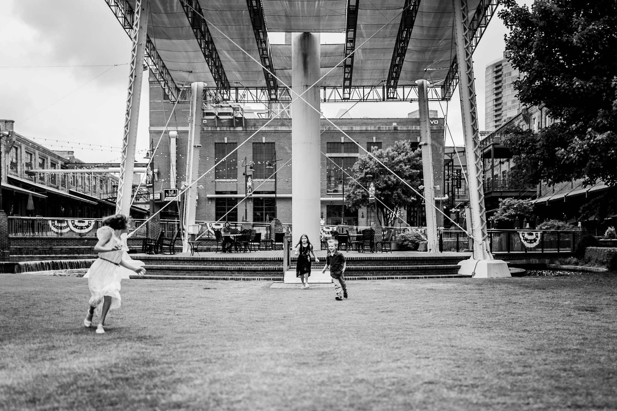 Durham Family Photographer | By G. Lin Photography | Candid black and white photo of kids running on grass at American Tobacco Campus