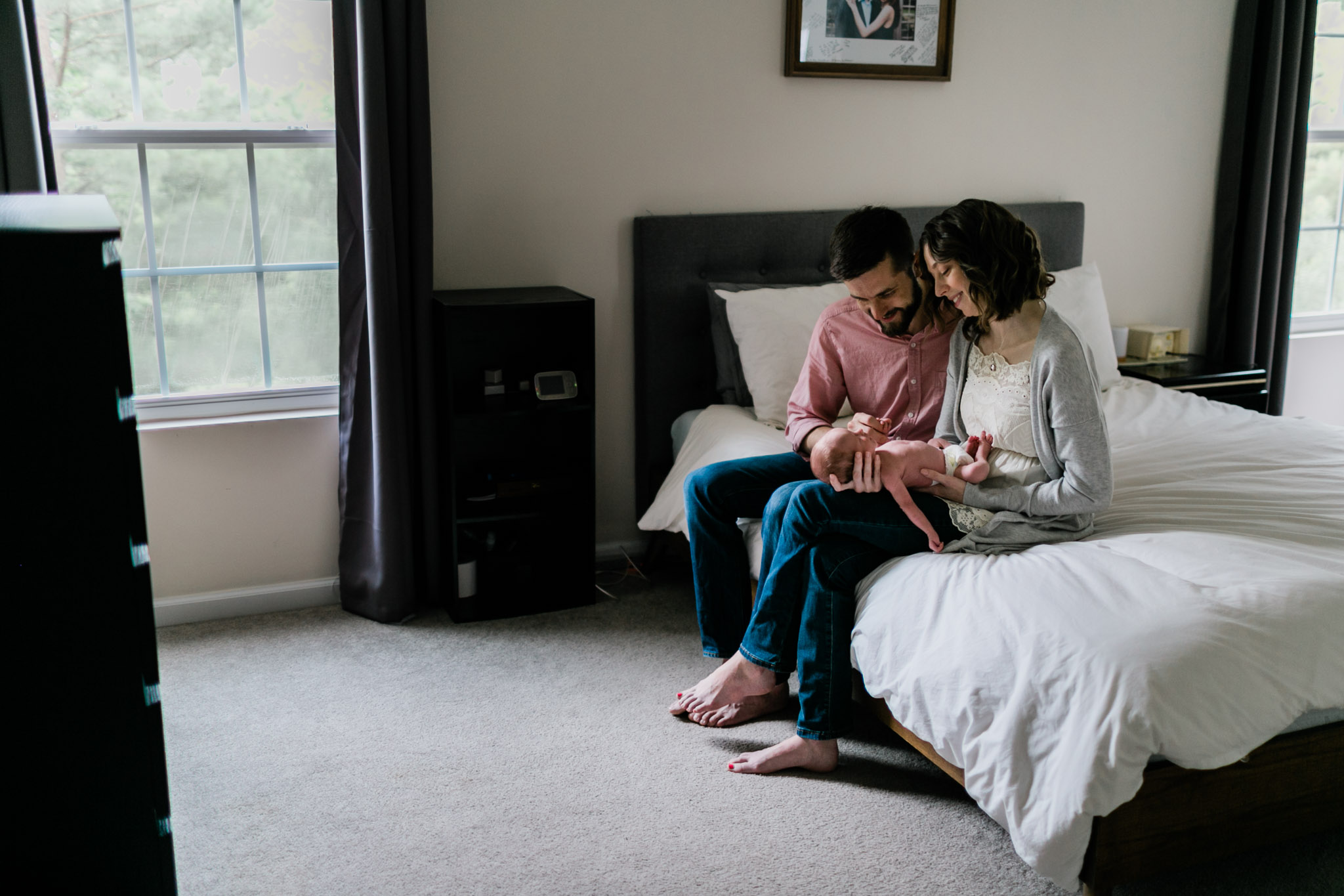Lifestyle Newborn Photography in Durham | By G. Lin Photography | Wide shot of parents holding baby in their arms on bed