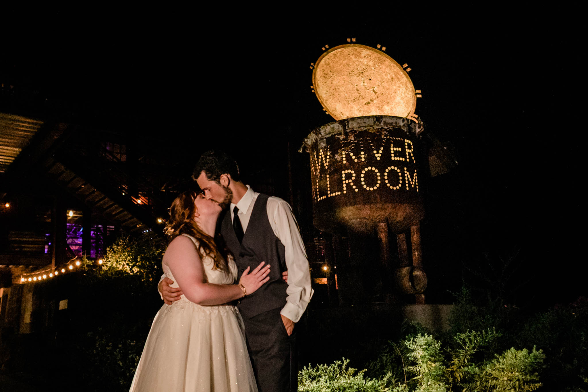 Haw River Ballroom Wedding | Durham Wedding Photographer | By G. Lin Photography | Evening shot of bride and groom outside kissing in front of Haw River Ballroom tank