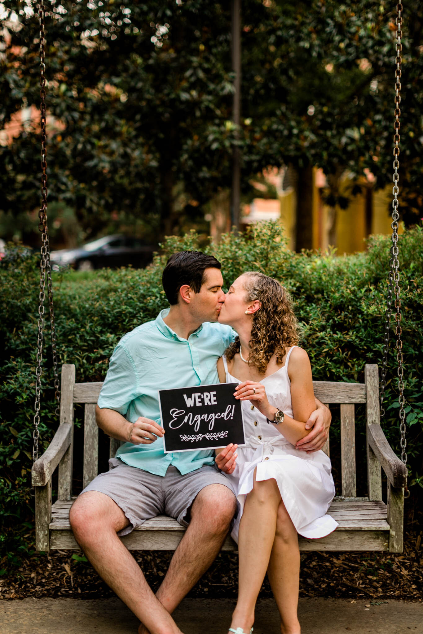 Raleigh Engagement Photographer | NC State University | By G. Lin Photography | Couple sitting on bench and holding engagement sign