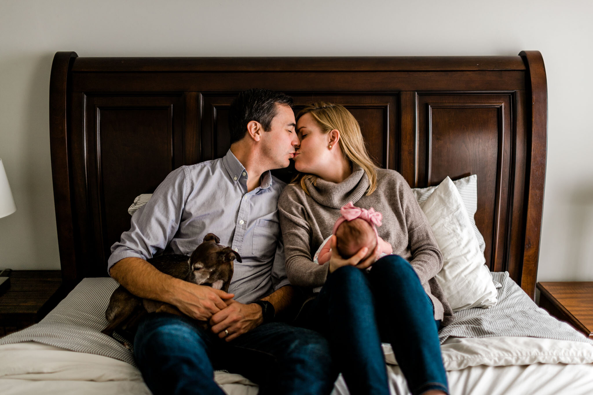 Parents kissing on bed while holding baby girl | Raleigh Newborn Photographer | By G. Lin Photography