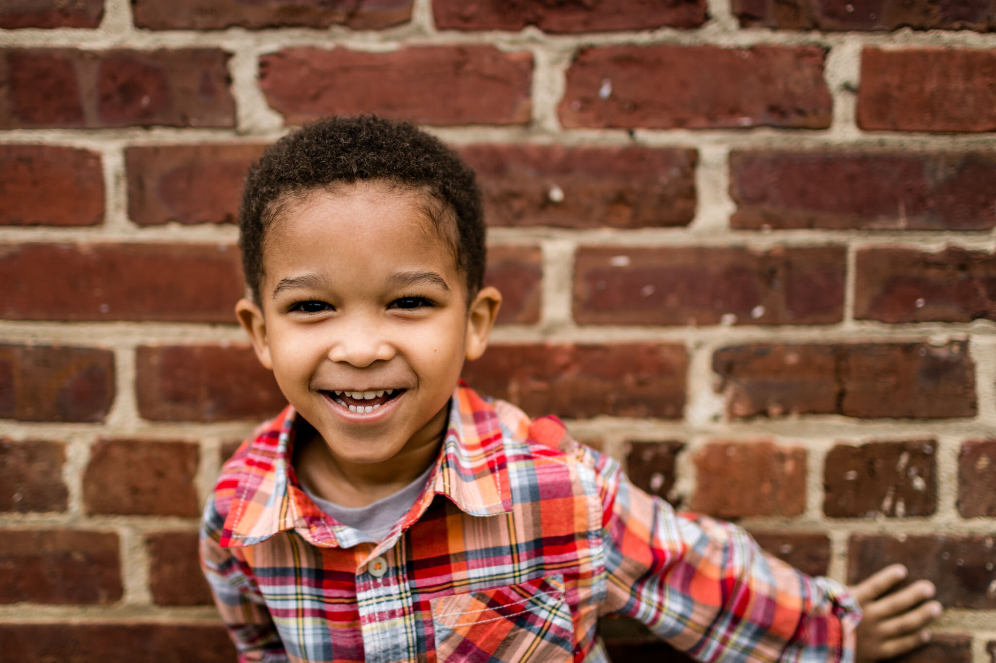 Toddler boy laughing and standing against brick wall | Durham Family Photographer | By G. Lin Photography