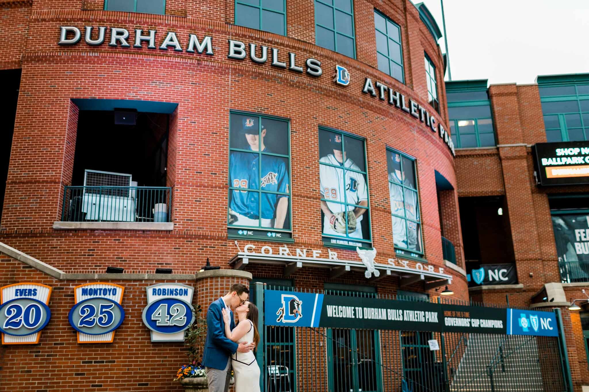 Durham Engagement Photographer | By G. Lin Photography | Couple kissing in front of Durham Bulls Stadium