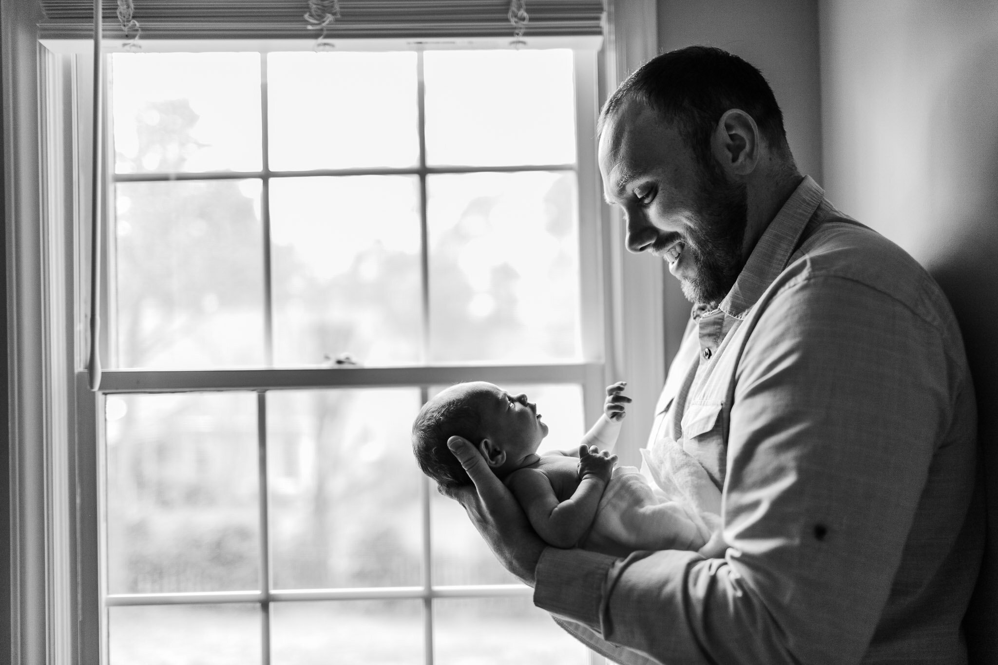 Raleigh Newborn Photographer | By G. Lin Photography | Black and white image of father holding baby girl by window