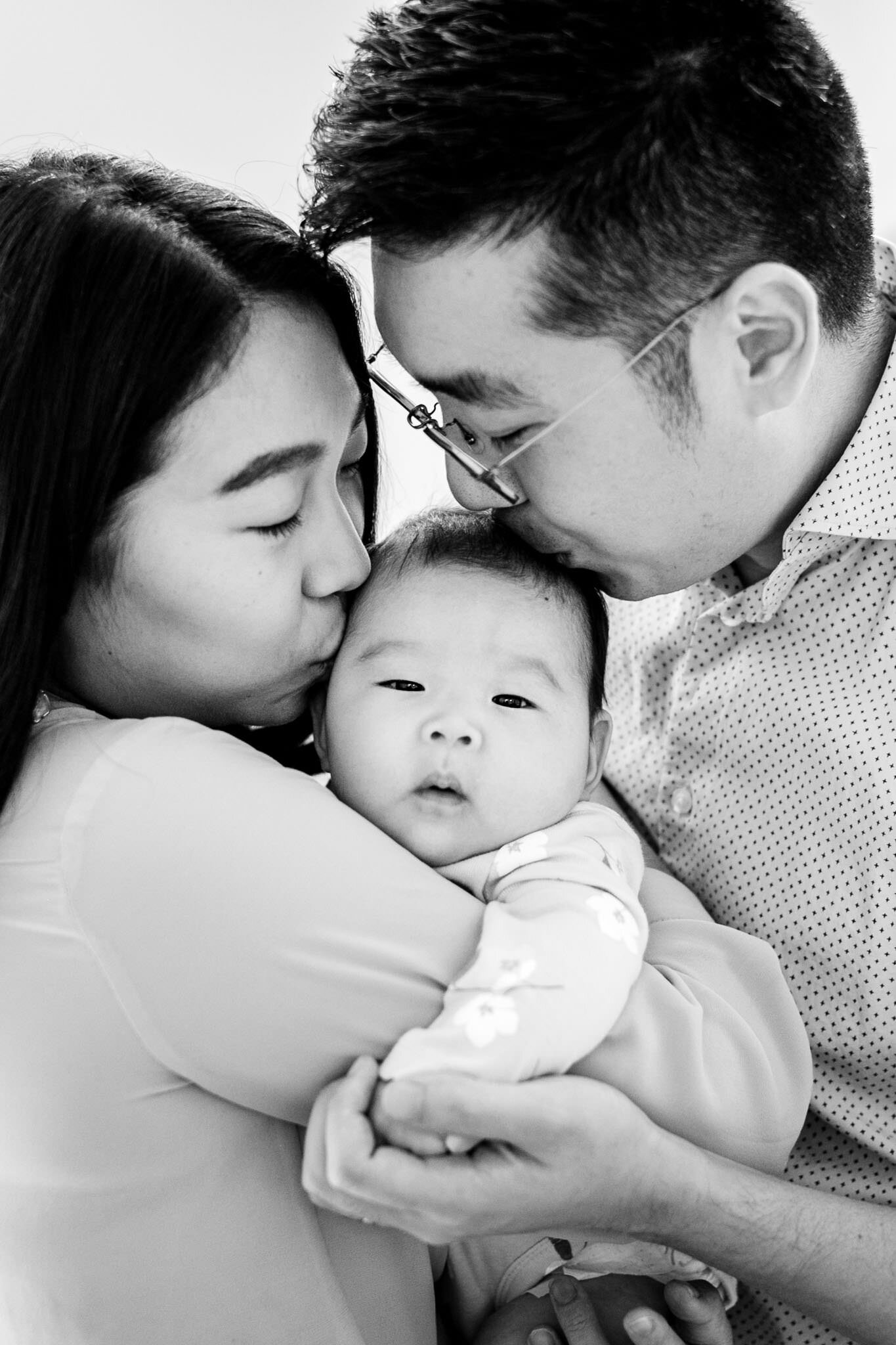 Raleigh Newborn Photographer | By G. Lin Photography | Black and white photo of mom and dad kissing baby girl