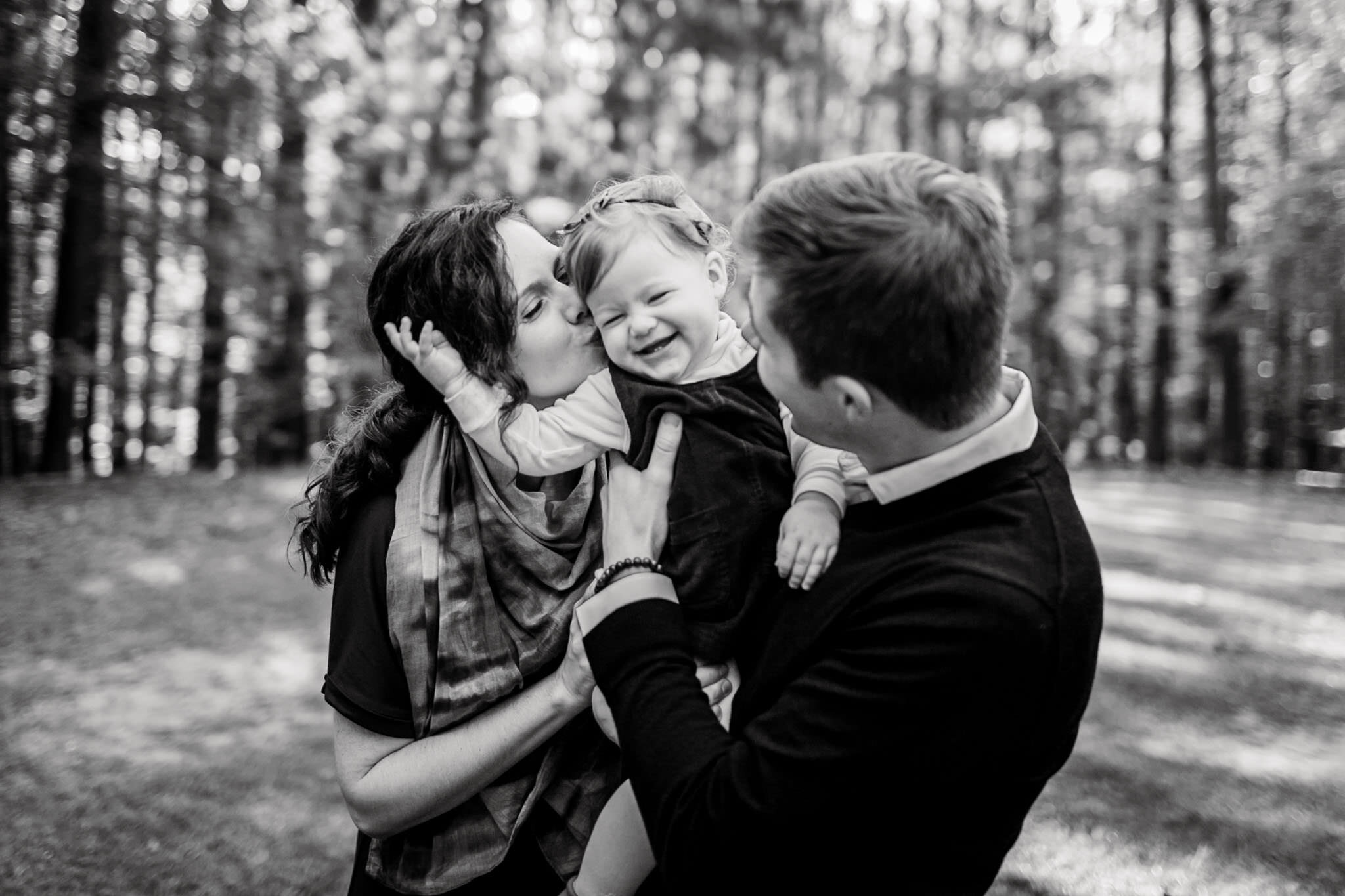 Raleigh Family Photographer | By G. Lin Photography | Umstead Park | Black and white photo of parents kissing baby girl