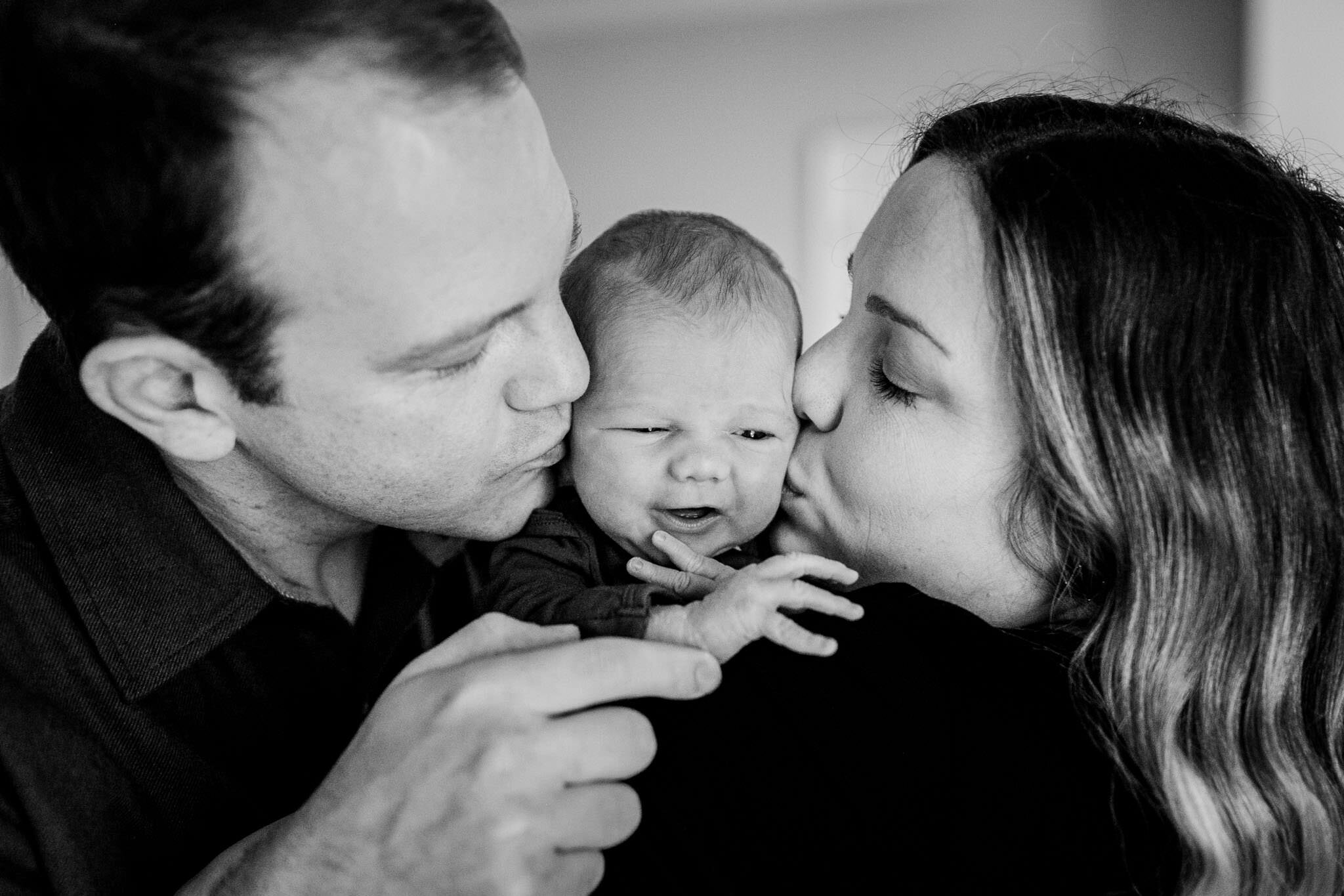 Raleigh Newborn Photographer | By G. Lin Photography | Black and white photo of mother and father kissing baby on the cheeks