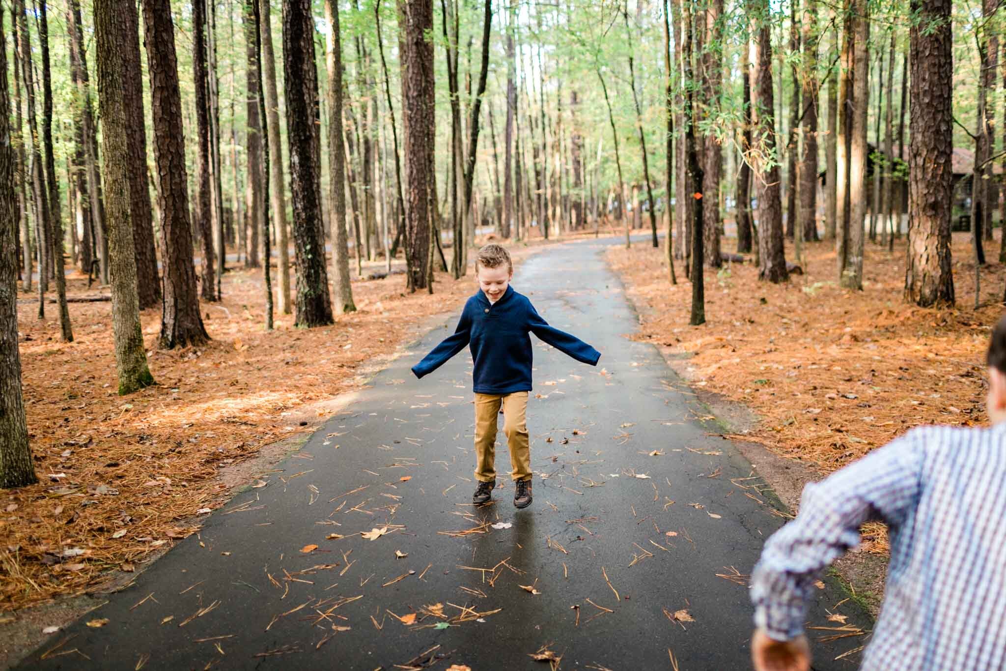 Raleigh Family Photographer | By G. Lin Photography | Umstead Park | Young boy walking backwards on paved path in forest