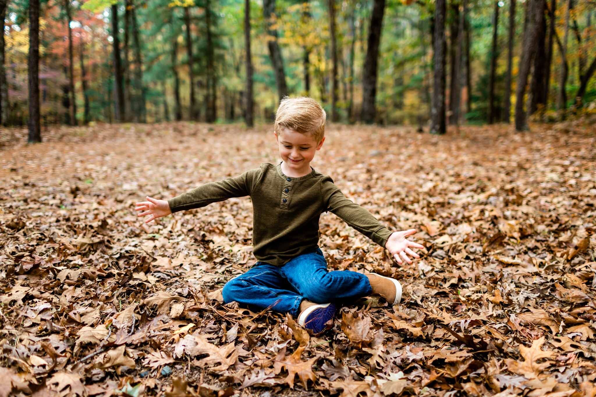 Raleigh Family Photographer at Umstead Park | By G. Lin Photography | Happy young boy sitting on leaves
