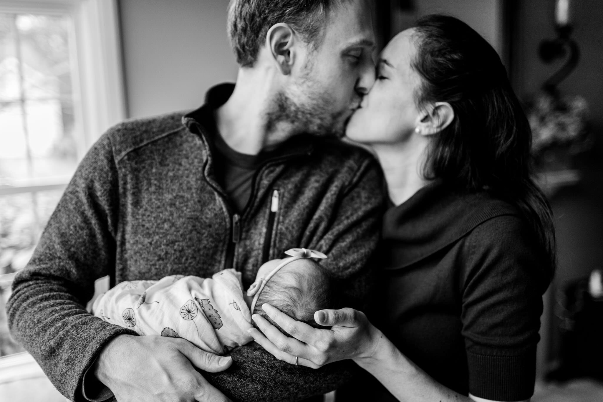 Durham Newborn Photographer | By G. Lin Photography | Black and white image of man and woman kissing while holding baby girl