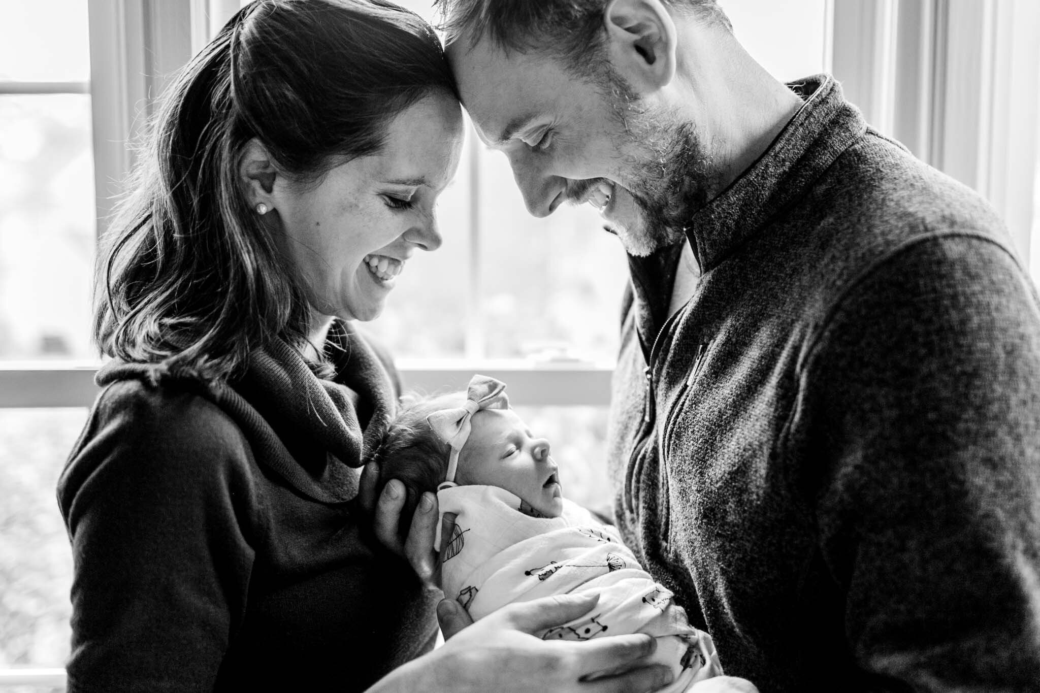 Durham Newborn Photographer | By G. Lin Photography | Black and white image of man and woman holding baby while standing in front of large window