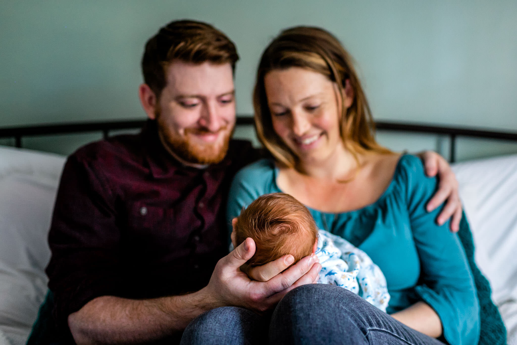 Durham Newborn Photographer | By G. Lin Photography | Mother and father sitting on bed looking at baby girl