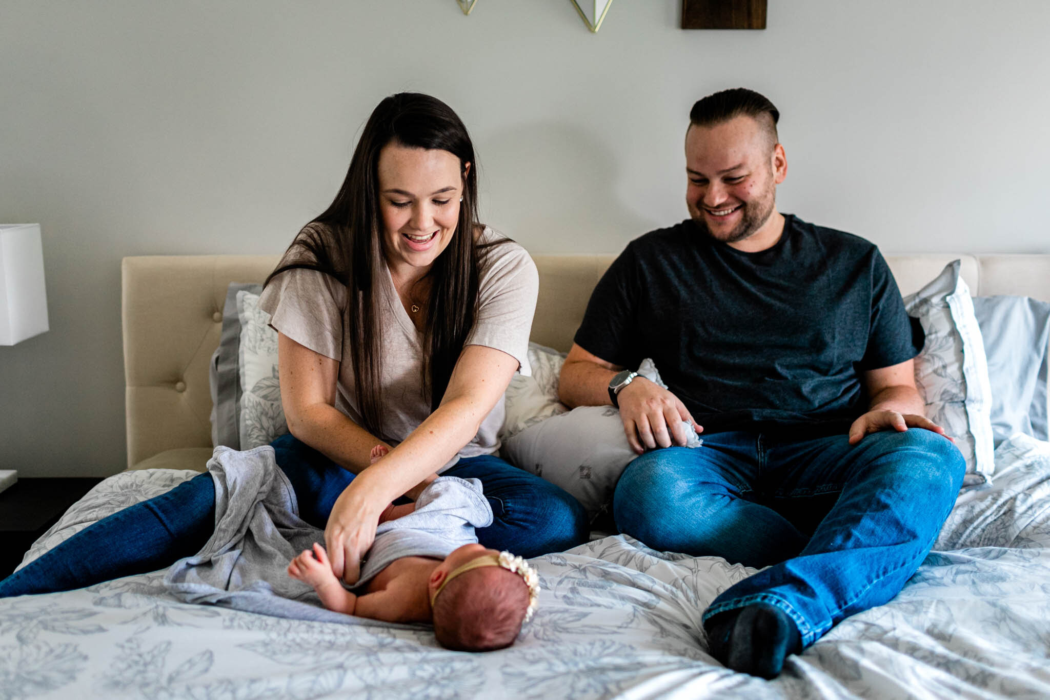 Parents sitting on bed and swaddling baby girl | Holly Spring Newborn Photographer | By G. Lin Photography