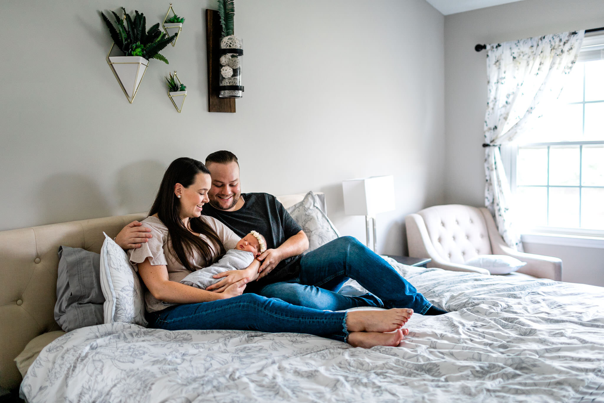Beautiful wide shot of couple sitting on bed holding baby | Holly Spring Newborn Photographer | By G. Lin Photography | Lifestyle newborn photography at home