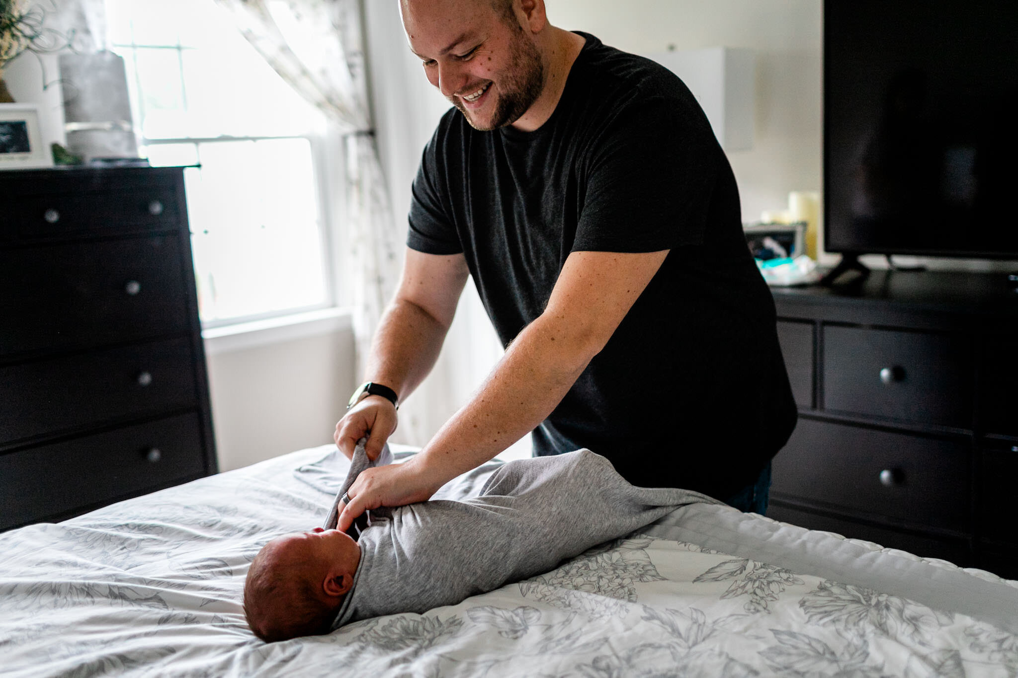 Father swaddling baby on the bed | Holly Spring Newborn Photographer | By G. Lin Photography