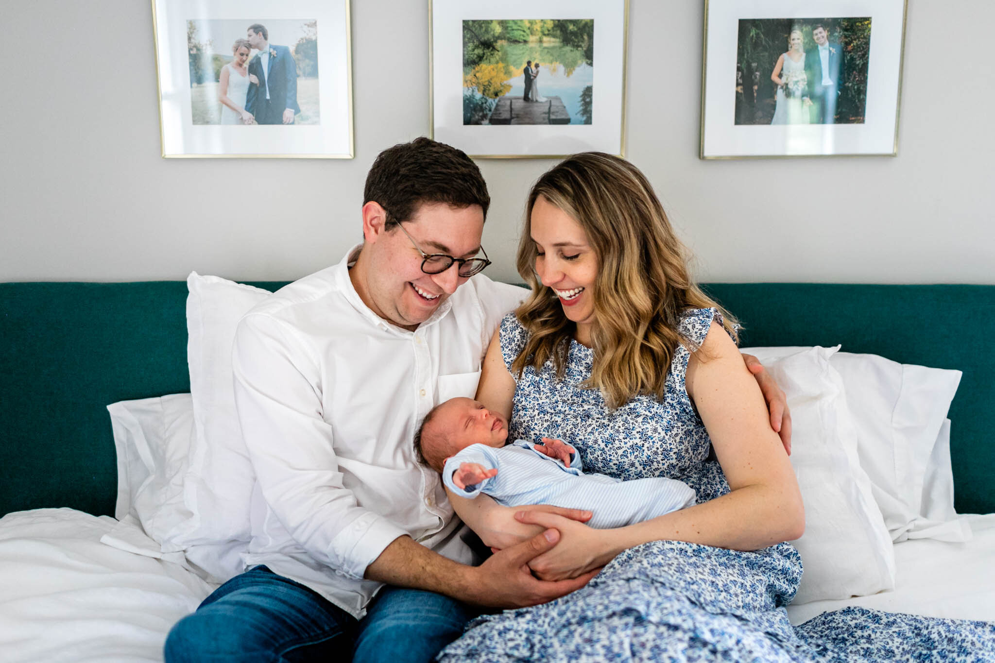 Couple sitting on bed with baby in their arms | Lifestyle newborn photography at home | Greensboro Newborn Photographer | By G. Lin Photography