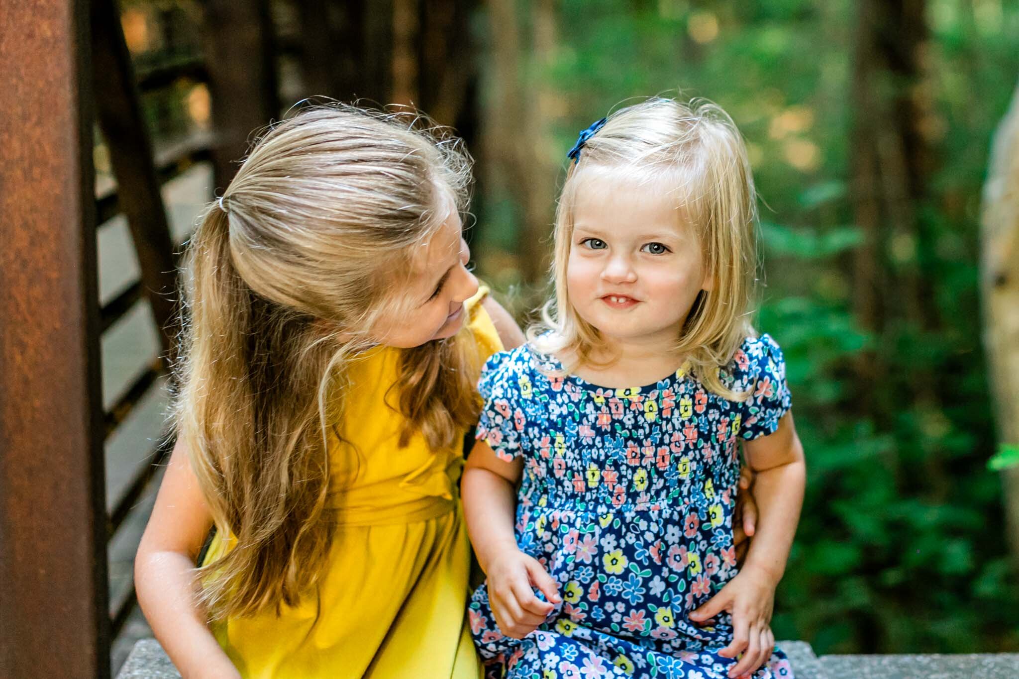 Young sisters smiling and sitting outside | Cary Family Photographer | By G. Lin Photography