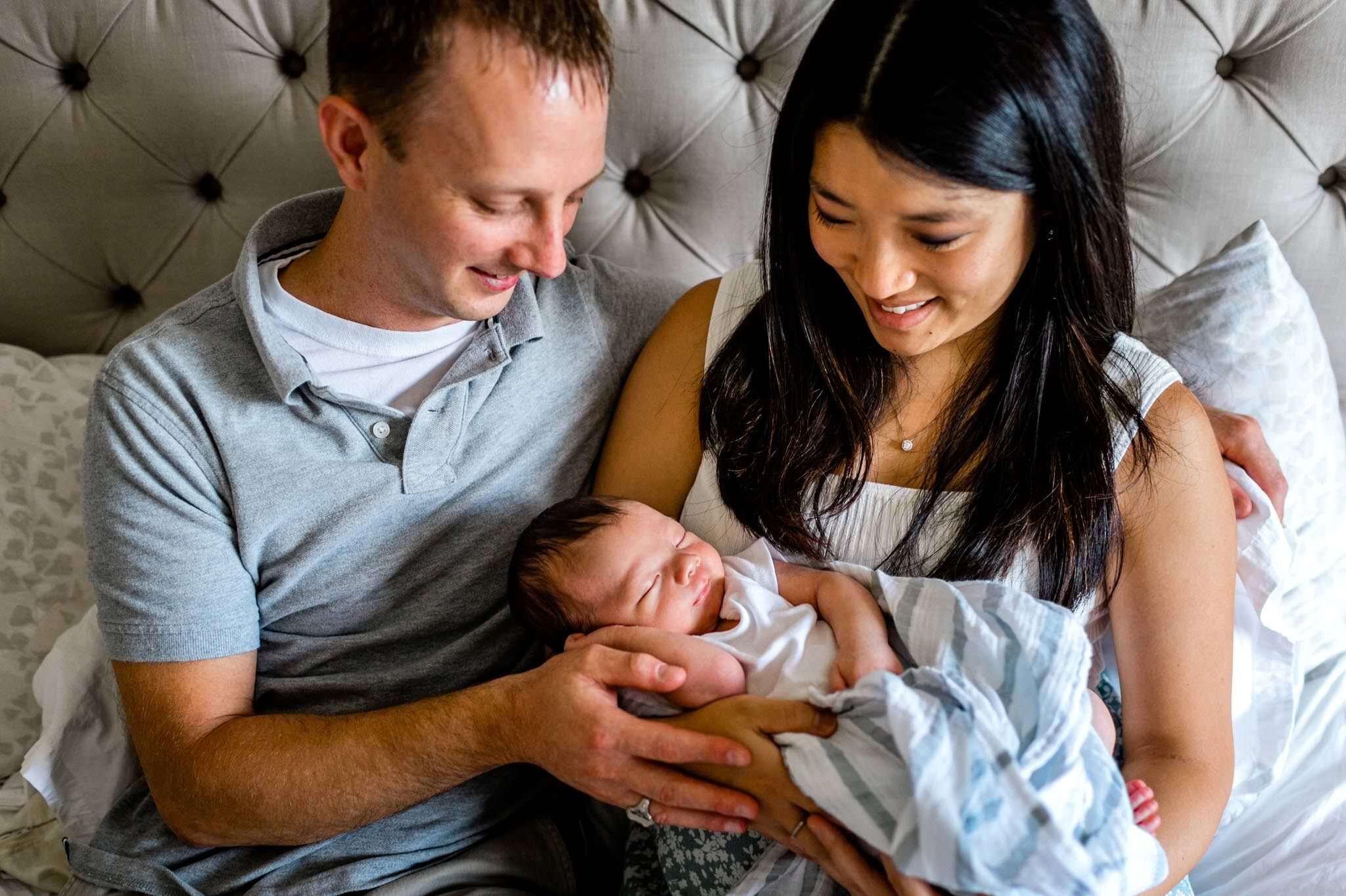 Durham Newborn Photographer | By G. Lin Photography | Father and mother holding baby and sitting on bed