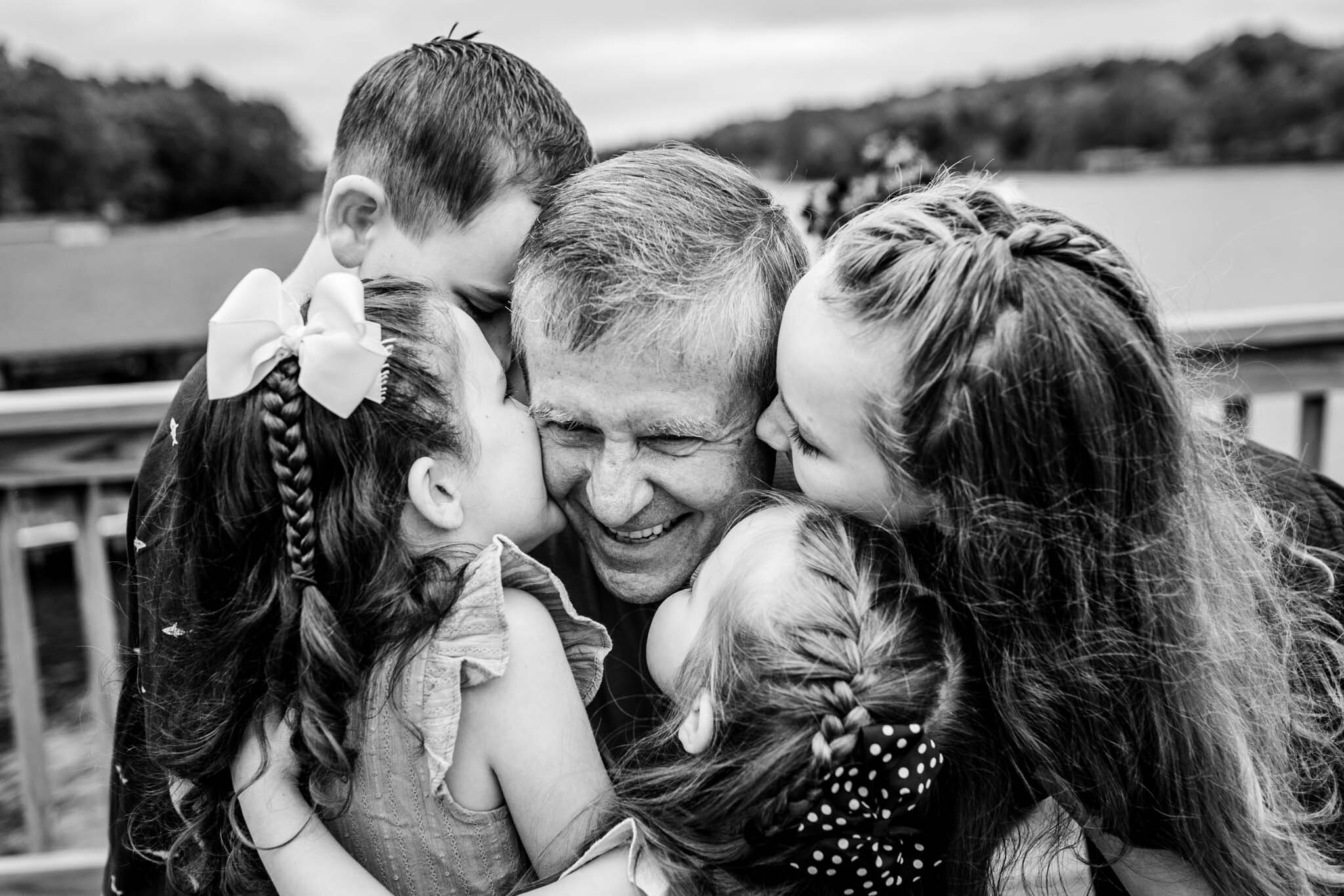 Beautiful black and white photo of four grandchildren kissing their grandpa | Lake Gaston Family Photographer | By G. Lin Photography