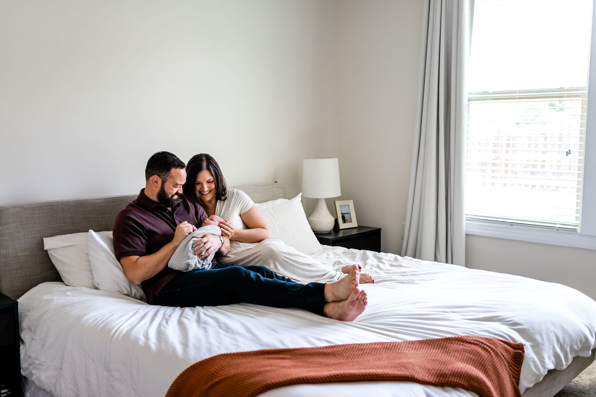 Durham Newborn Photographer | By G. Lin Photography | Father and mother holding baby girl while sitting on bed