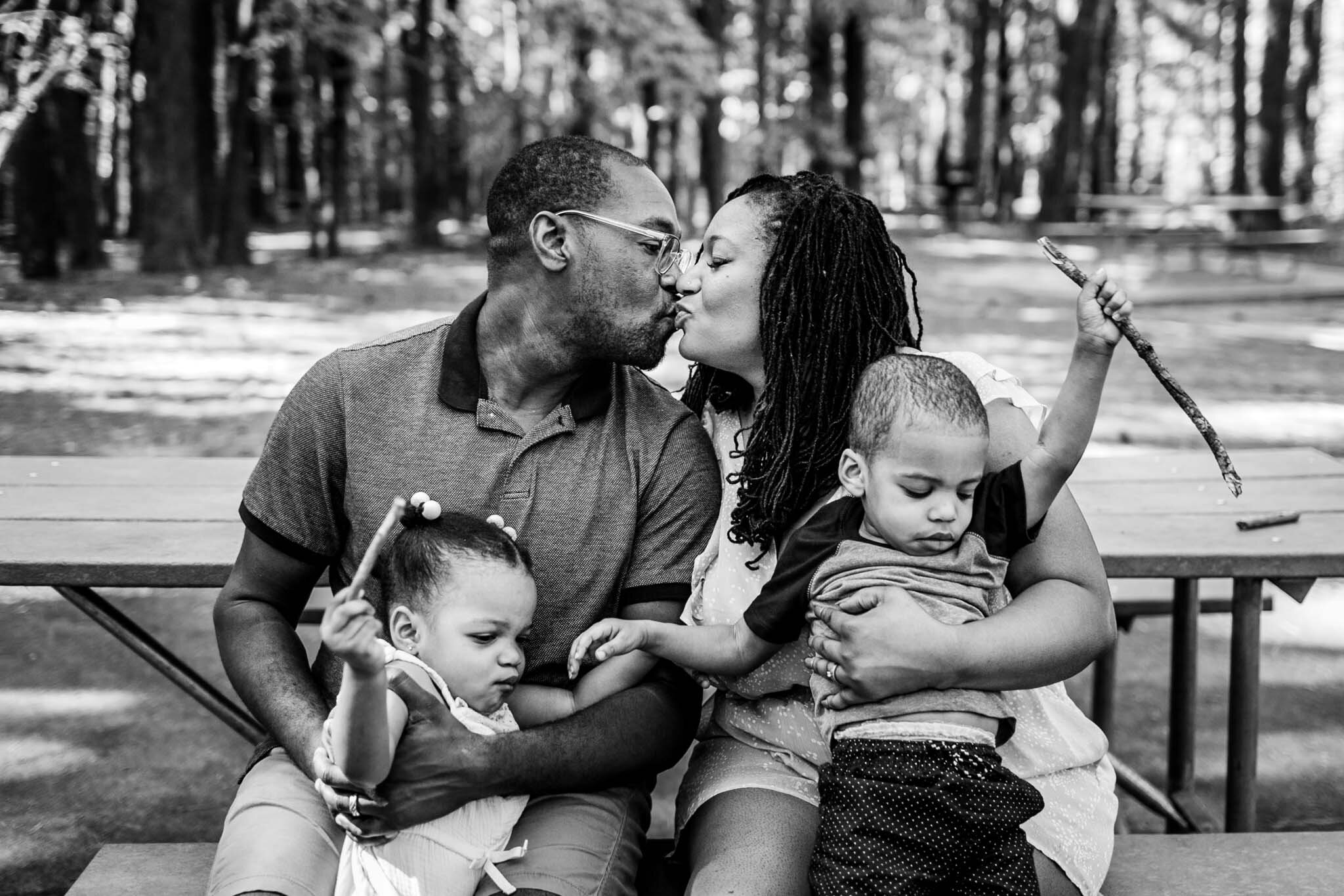 Raleigh Family Photographer | By G. Lin Photography | Umstead Park | Black and white photo of parents kissing and holding kids