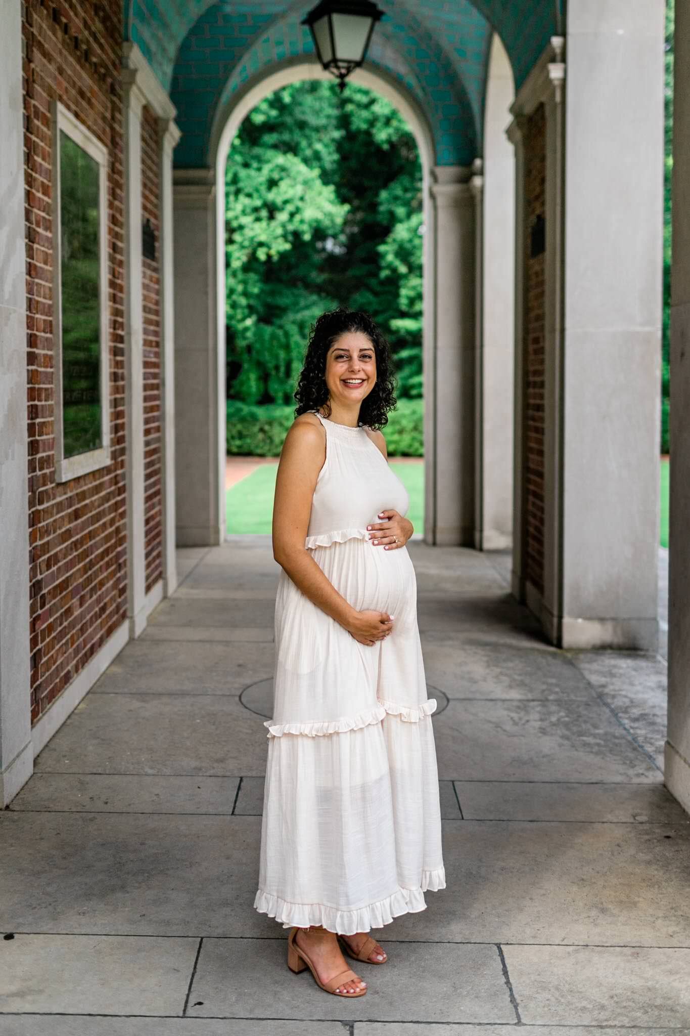 UNC Chapel Hill Maternity Photography | By G. Lin Photography | Pregnant woman smiling at camera and standing by the Bell Tower