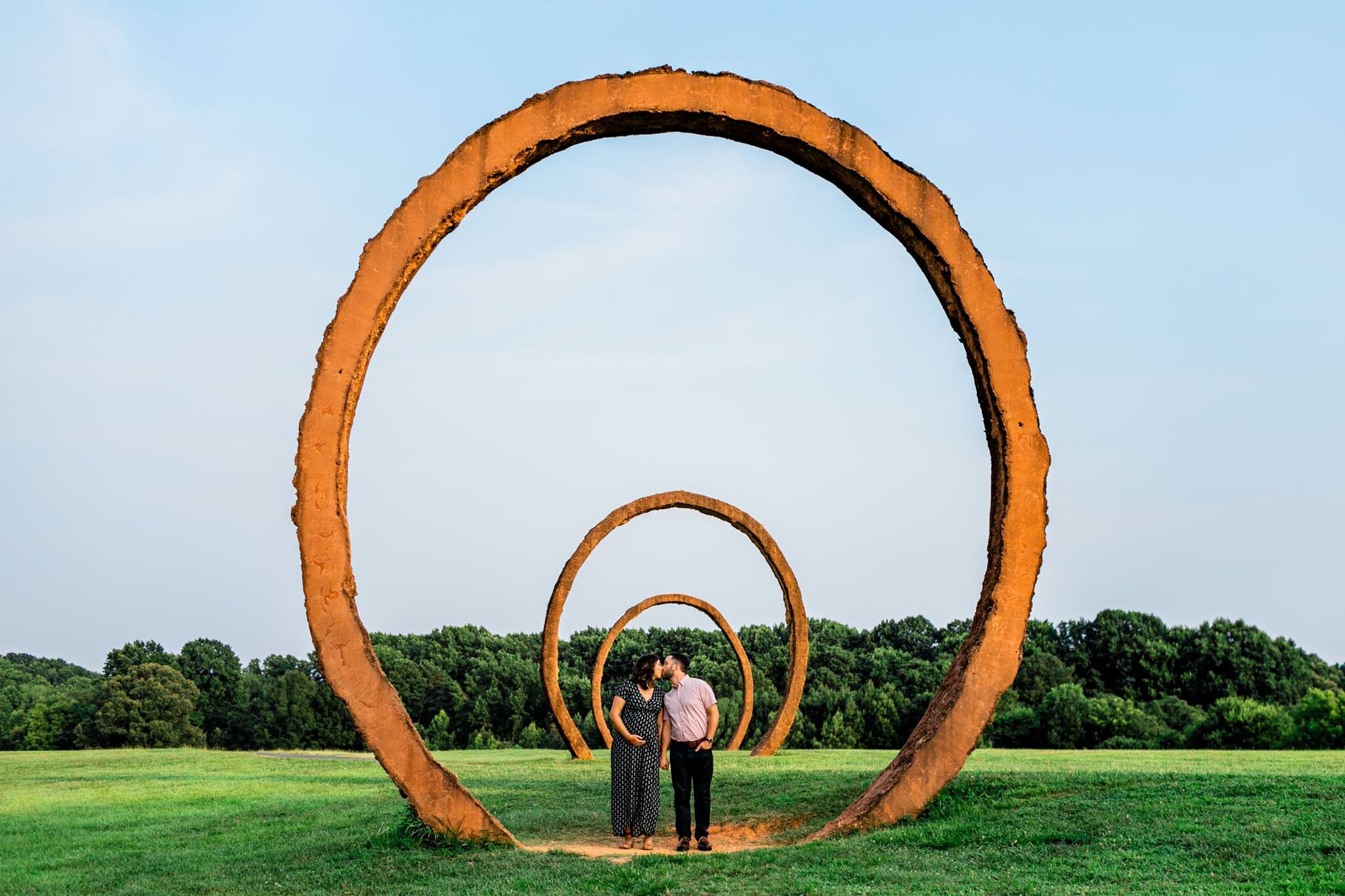 Raleigh Maternity Photographer | By G. Lin Photography | NC Museum of Art | Couple kissing underneath hoop rings art sculpture