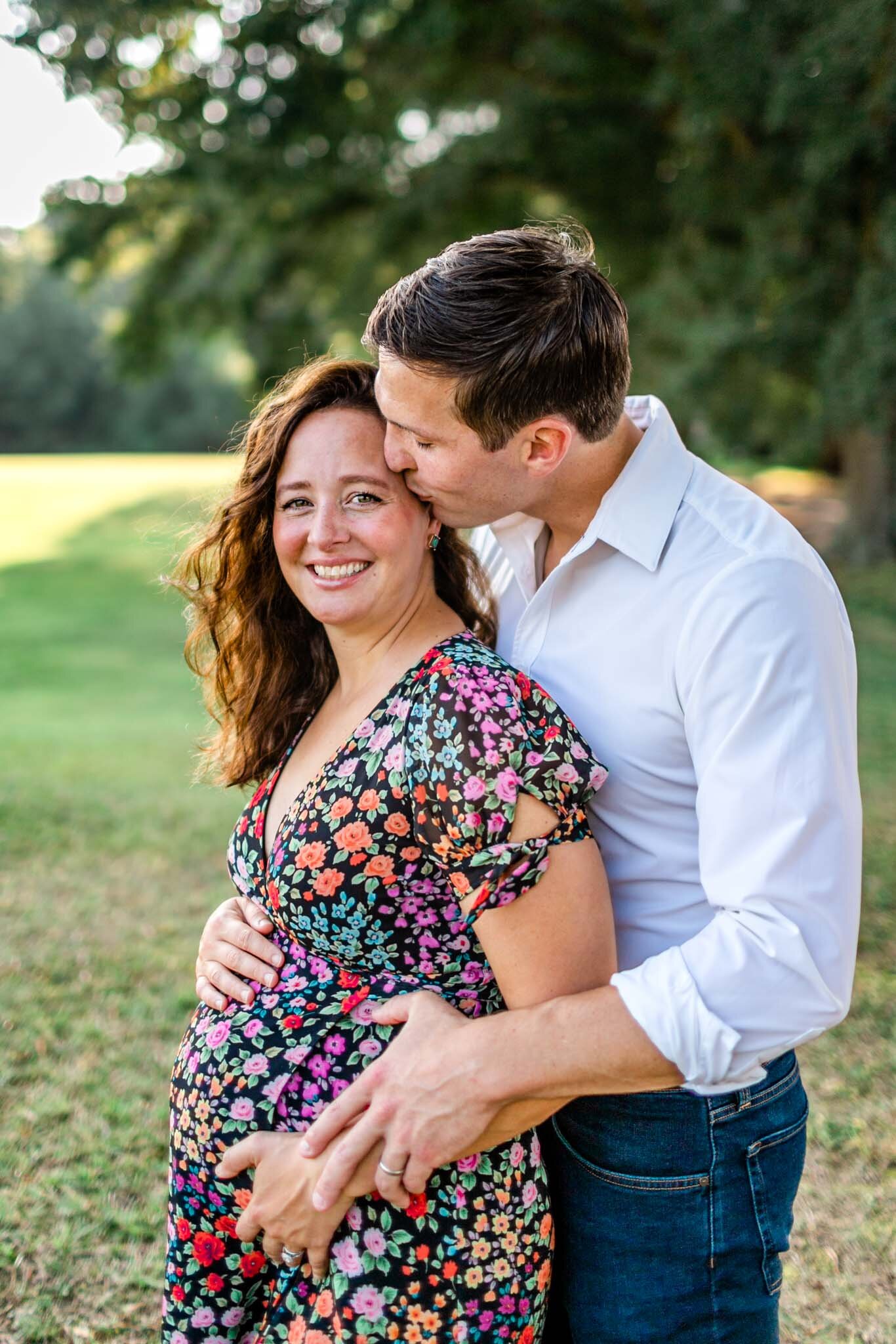Raleigh Maternity Photographer | Dix Park | By G. Lin Photography | Man embracing woman and giving her a kiss on the cheek
