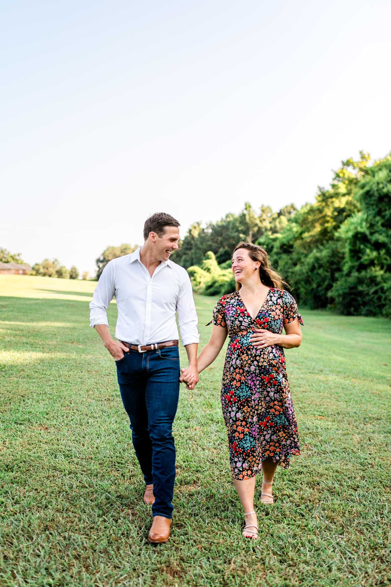 Raleigh Maternity Photographer | Dix Park | By G. Lin Photography | Man and woman holding hands and walking in open field while laughing