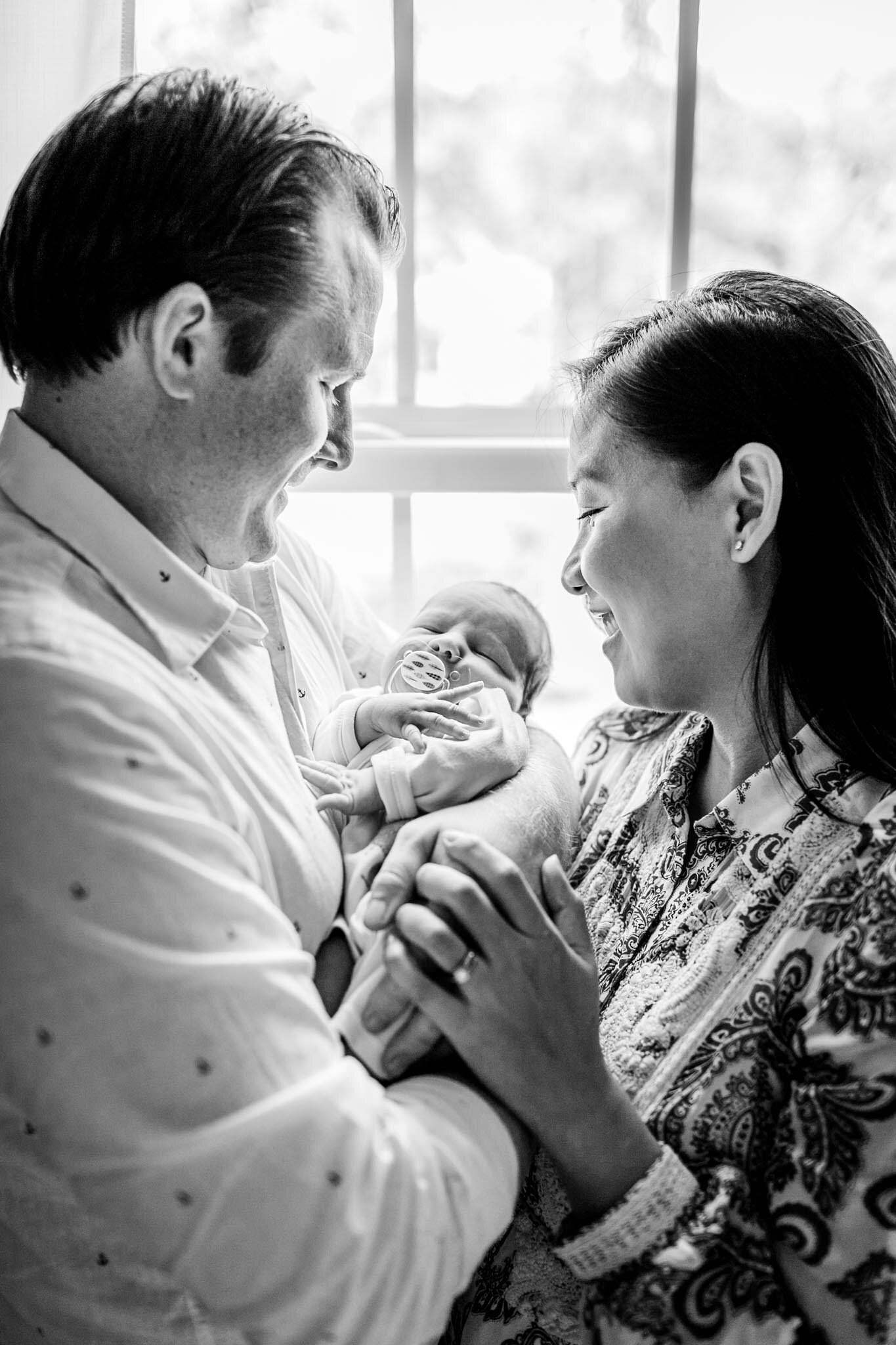 Pittsboro Newborn Photographer | By G. Lin Photography | Black and white photo of parents holding baby by window