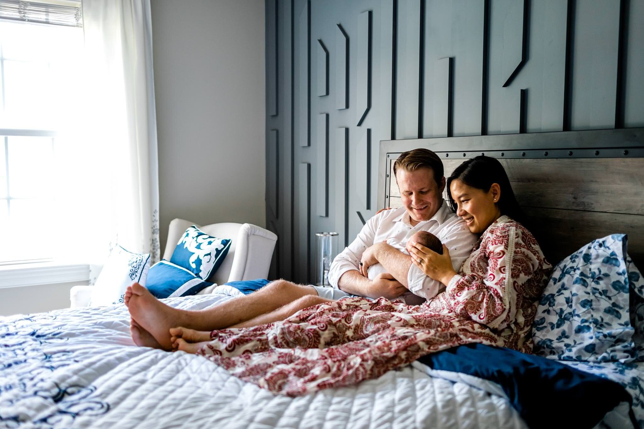 Pittsboro Newborn Photographer | By G. Lin Photography | Couple sitting on bed with newborn baby