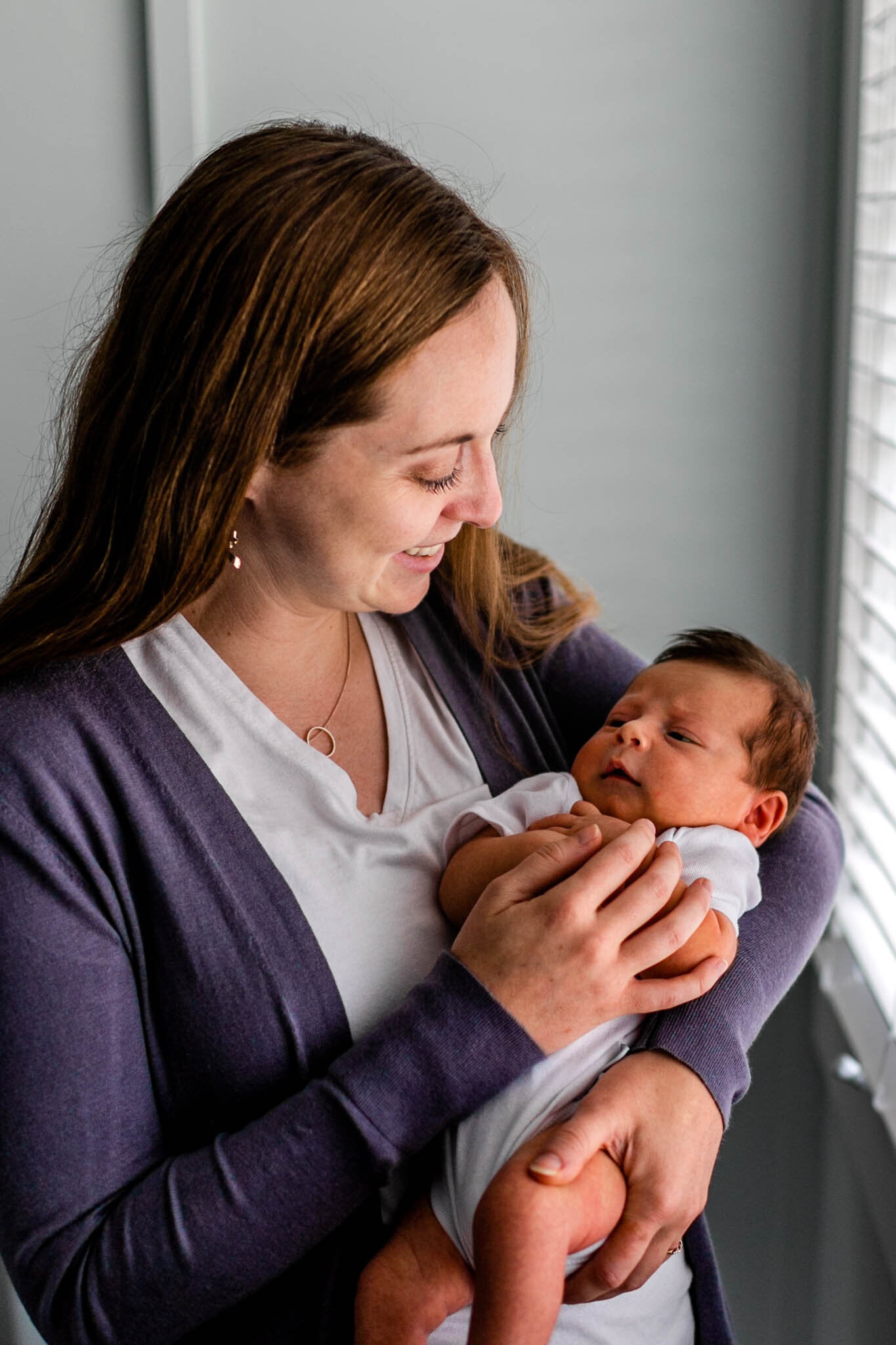 Durham Newborn Photographer | By G. Lin Photography | Mother holding baby by window and smiling