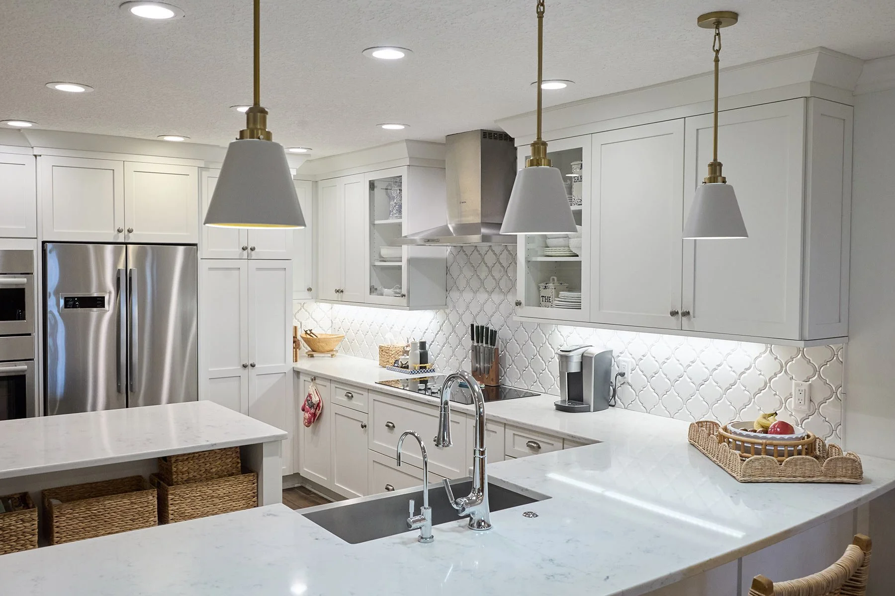 Modern white kitchen with hanging pendant lights, stainless steel appliances, white cabinets, and a marble countertop island