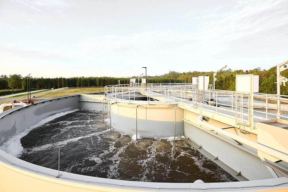 Elevated view of a wastewater treatment plant with circular clarifier tanks filled with water and mechanical equipment surrounded by railings.