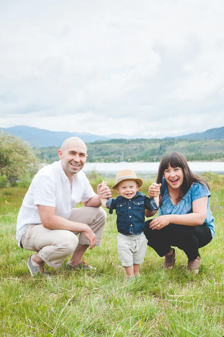 Mom and Dad get on their son's level and help him stand for a happy photo at their Lake Dillon family photo session, in the heart of the Colorado Rocky Mountains.