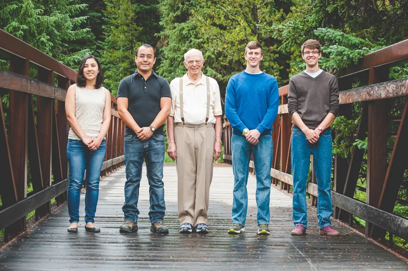 Grandpa and four grandchildren (all grown up) stand together on a bridge in the woods at Copper Mountain Resort for their family photo session.