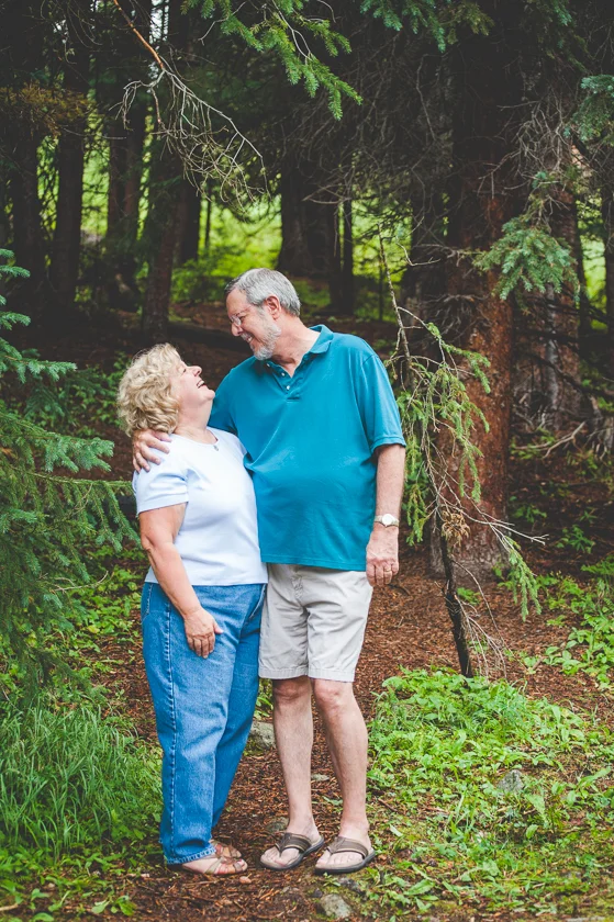 Husband and wife hug in close for a sweet photo during their family portrait session, in the wooded mountains near Breckenridge, Colorado.