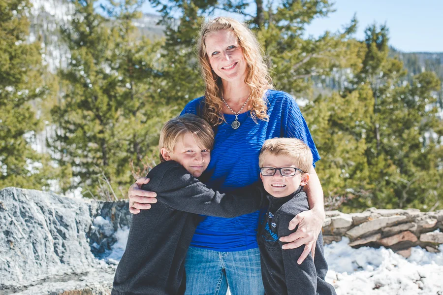 Mom and her two young boys hug in close during a wintery family photo session in the mountains near Breckenridge, Colorado.