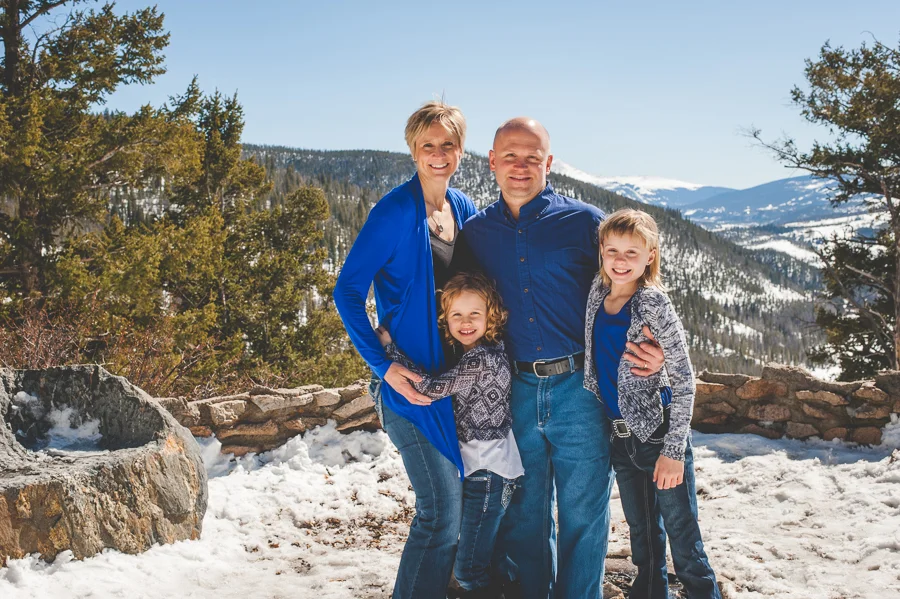 Mom, Dad and two daughters get close and warm up during a snowy photo session with the family in the mountains near Breckenridge, Colorado.