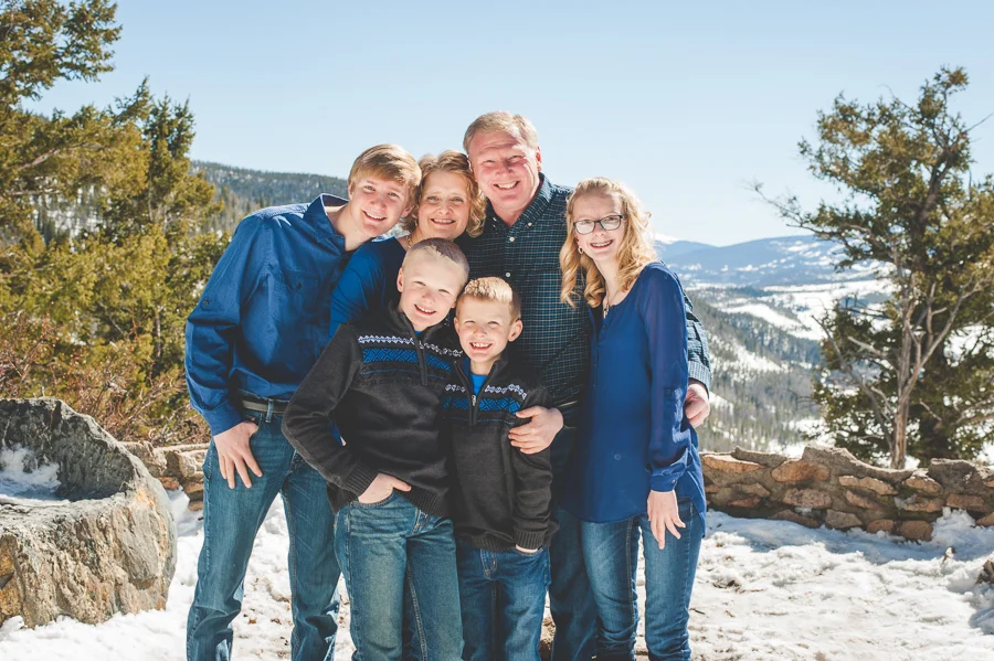 A family of six gathers close for their portrait at Sapphire Point, near Breckenridge, Colorado, with snow covered ground and mountaintops in the background.
