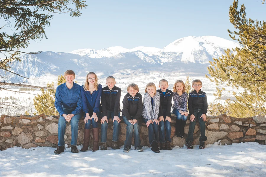 All the grandkids (eight grandchildren, to be exact!) sit side by side on a rock wall at Sapphire Point near Breckenridge, Colorado, overlooking Lake Dillon and Buffalo Mountain, during a winter family photo session.