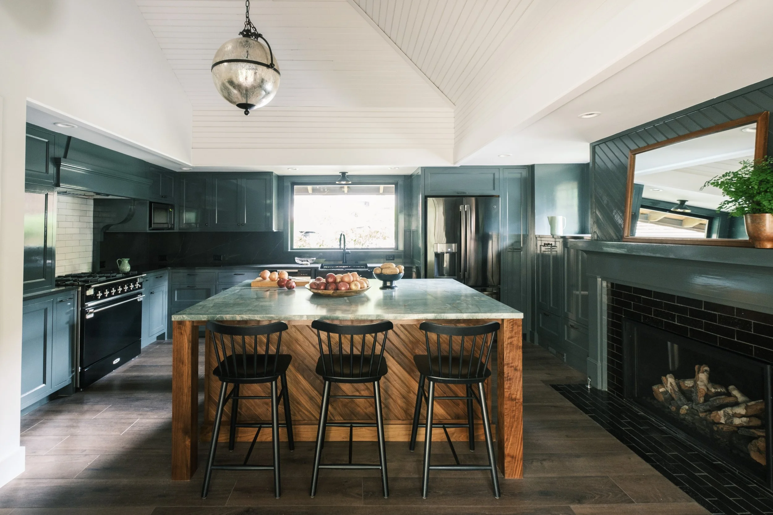 Piano Nobile residential kitchen with dark cabinetry, wood island, vaulted ceiling, and fireplace.