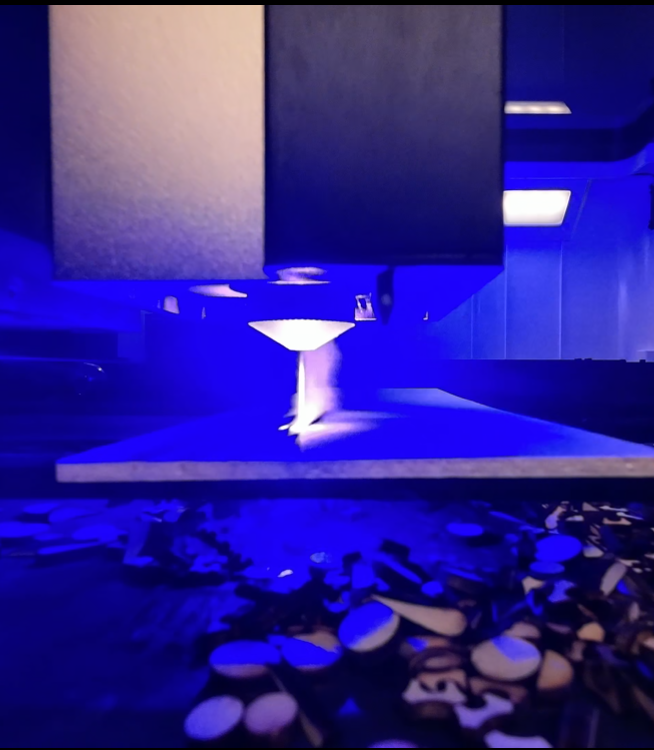 Close-up of a 3D printer creating a small object with blue UV light, with printed pieces scattered below.