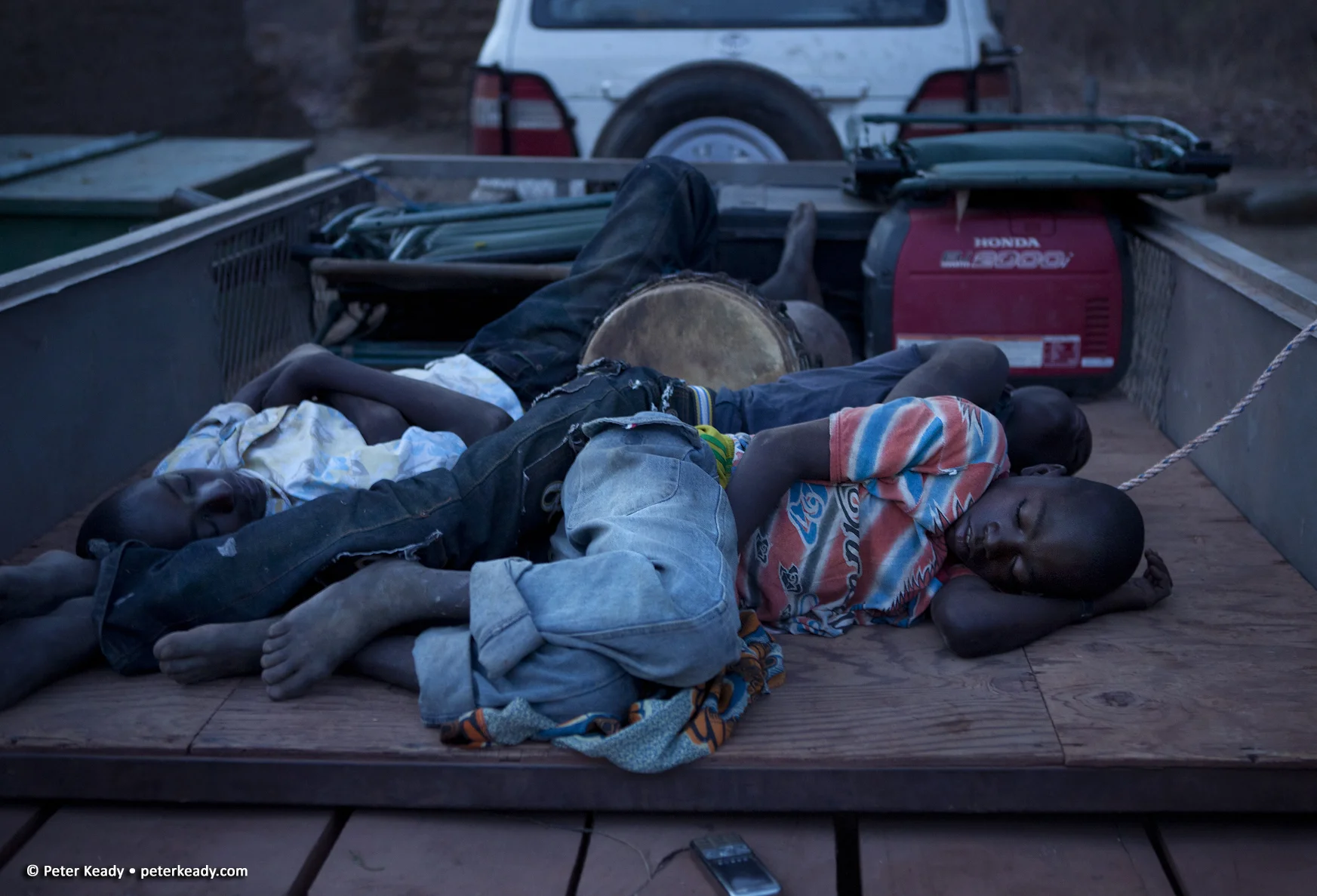 Young boys sleep in the bed of an equipment wagon in the early light of an African morning. Burkina Faso, Africa.