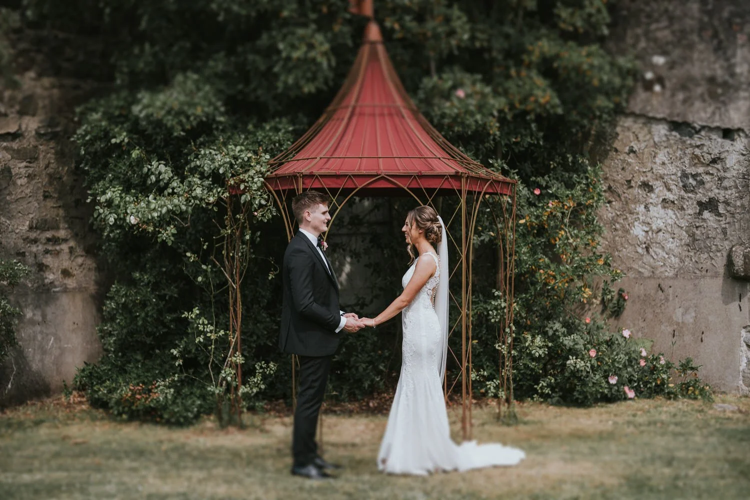 Bride and groom holding hands under the red roofed gazebo in the castle walls garden at Lissanoure Castle